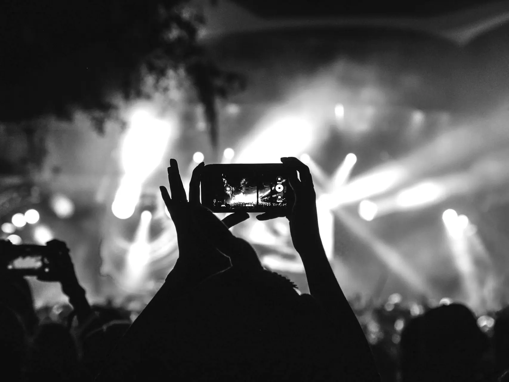 person holding smartphone taking video of a concert near stage with lights during nighttime